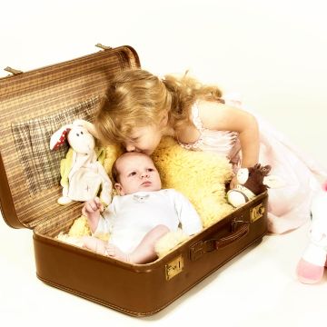 Baby im Koffer wird von der Schwester auf die Stirn geküsst