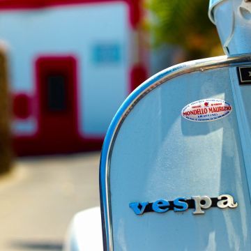 Blauer Vesparoller mit unscharfer weiß roter Hausfassade